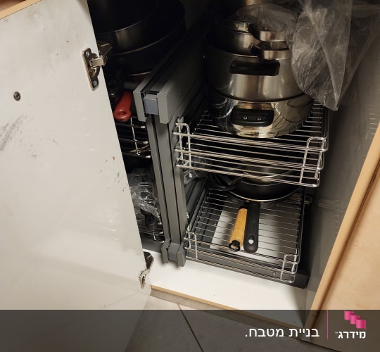 ארון מטבח פתוח עם סירים ומחבתות על מדפים נשלפים